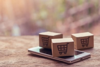 online shopping - paper cartons or parcel with a shopping cart logo and smartphone on wood table top. shopping service on the online web and offers home delivery.