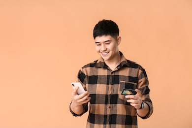asian man with credit card and mobile phone on color background