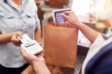 close up of woman in store making contactless payment at sales desk holding credit card to reader