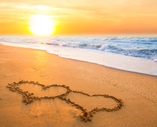 two hand drawn hearts on beach sand over sunset