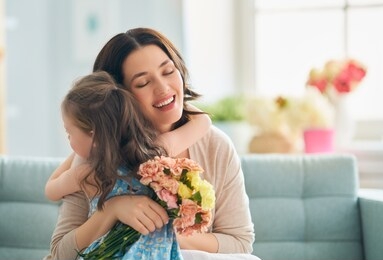 happy mother's day! child daughter congratulates mom and gives her flowers. mum and girl smiling and hugging. family holiday and togetherness.