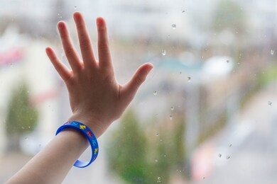 child's hand in an autism bracelet against a window, world autism awareness day, concept