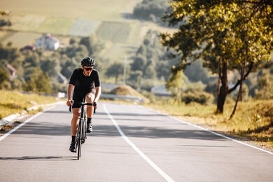 front view of bearded man with athletic body shape in protective helmet and glasses riding bicycle with beautiful nature around. concept of self discipline and motivation.