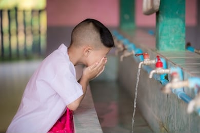 handsome kid boy use their hands to clean water from their faucets and wash their faces after a run in the hot sun. children aged 5-6 years.