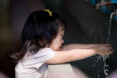 asian girl was using water to wash her hands, she closed her eyes because of water splashing into her face. she is wearing a white shirt. happy children's lovely girl aged 3-4 years old.