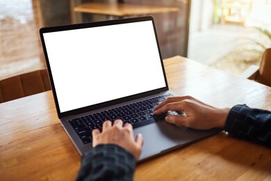 mockup image of a woman using and typing on laptop computer with blank white desktop screen on wooden table