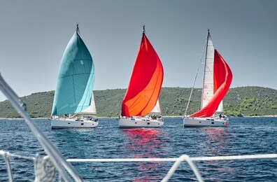 sailboats compete in a sail regatta at sunset, view throug the ropes, race of sailboats, reflection of sails on water, multicolored spinnakers, island is on background, clear weather