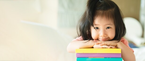 panoramic of asian toddler portrait put her chin and smiling over her hands on stack of books, concept little bookworms joy learning to be intelligent kids, adorable child reading book for preschool.