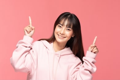 young beautiful asian woman smile with clean and fresh skin happiness and cheerful with positive emotional pointing up,isolated on pink background,beauty cosmetics and spa treatment concept