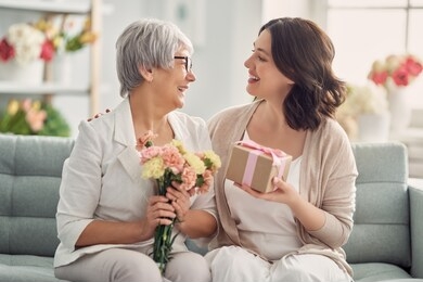 happy mother's day! beautiful young woman and her mother with flowers and gift box at home. 