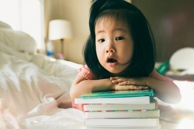 image of asian toddler portrait shot while her proud and talking to present her book stack, concept little bookworms enjoy learning to be intelligent kids, adorable child reading book for preschool.
