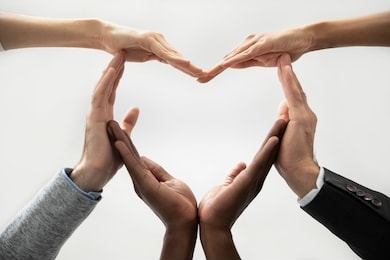 close up bottom view concept of diverse business people join hands forming heart. show unity and support, protection of business. multiracial colleagues involved in team building activity for charity.