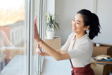 waist up portrait of young asian woman washing windows while enjoying spring cleaning in house or apartment, copy space
