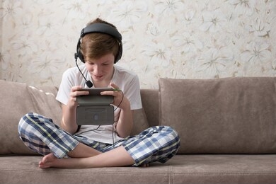 teenager sits in lotus position on the couch and watches video on the phone. boy playing on the phone