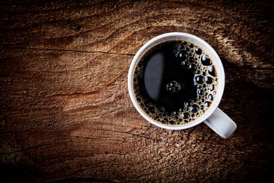close up overhead view of a cup of strong frothy espresso coffee on a rough textured wooden surface with dark vignetting and a highlight around the mug, with copyspace
