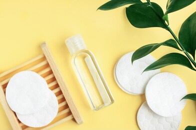 herbal dermatology cosmetic skin care lotion in bottle, cotton pads, fresh green leaf over light yellow empty table background. organic beauty treatment products. 