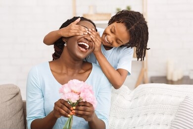 surprise concept. laughing african woman holding flowers, little girl covering her eyes, copyspace