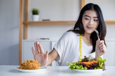 woman choose to eat healthy vegetables and refuse to eat fried chicken. woman on dieting for good health concept. young woman rejecting junk food and choosing healthy food fresh vegetable.