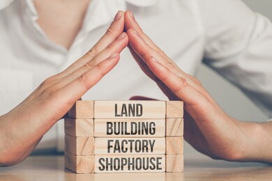 real estate insurance concept - hands over wooden blocks with the inscriptions land, building, factory, shophouse. close up.