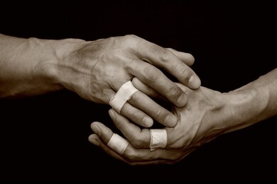 dirty, sinewy male hands with bandaged, damaged fingers on a black, isolated background. the concept of hard work of a miner, mechanic, worker. tinted photo.