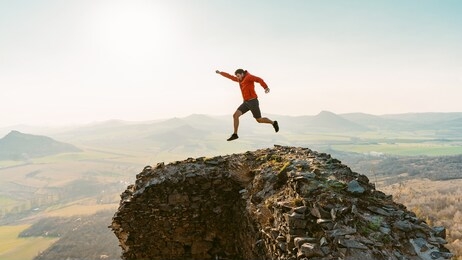 young happy man high jumping on castle ruins. admires the beauty of nature. looks at the horizon. sunny spring day