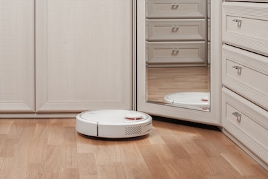 reflection of white robot vacuum cleaner running before mirror in bedroom. modern smart appliance for cleaning house.