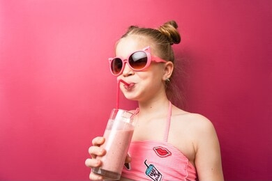 vibrant colors: a girl in sunglasses in a pink bathing suit drinks a cocktail through a pink straw and exclaims in surprise.