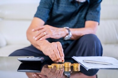 elderly man stacking golden coins with a calculator and document on the table