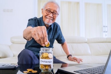 happy senior man savings golden coins in a jar with retirement text and laptop on the table