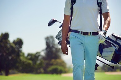 golf player walking and carrying bag on course during summer game golfing