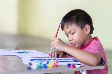 selective focus. portrait image of 5 yeas old child boy. asian student drawing and painting colours on the paper in the room. study​ from​ home, social​ distancing, kid and education concept.