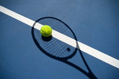 the shadow of the tennis racket and the tennis ball inside it. all on a blue tennis court.
