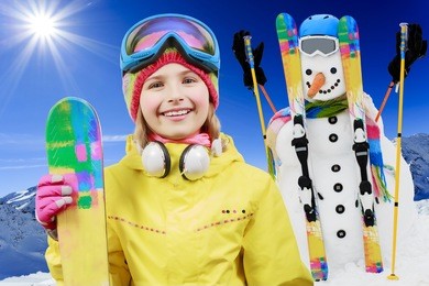 ski, skier, sun and winter fun - skier girl with snowman enjoying winter holidays