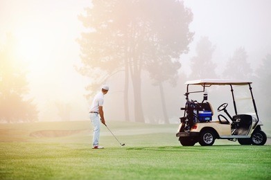 golfer lining up shot with iron club on golf course in fairway at sunrise