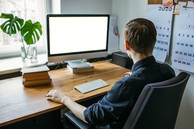 man working from home office. computer with blank empty screen for copy space and information. businessman from behind shoulder view. a creative entrepreneur