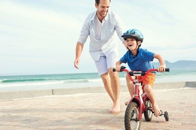 father and son learning to ride a bicycle at the beach having fun together