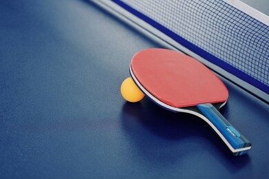 close-up image of ping-pong racket and orange ball ion table with net