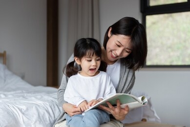 young asian mother is reading a book with her daughter