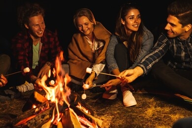 photo of a young happy positive group of friends at night holding marshmallow in fire outdoors.