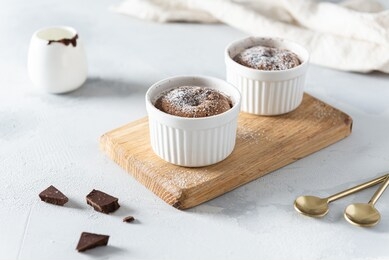 warm dessert chocolate fondant lava cake with sugar powder in ceramic molds on wooden board. restaurant, bakery, confectionery menu, recipe. side view, horizontal