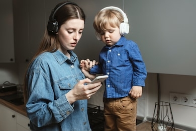a young mother with a son listening to the music in the kitchen. mom and a baby listening to the music on the smartphone and  watching a video. lifestyle.