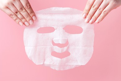 female hands hold white fabric mask on pink background.