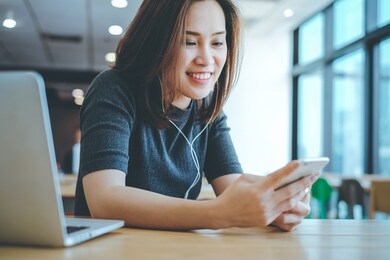 young happy asian millennial woman listening music with her smartphone and wearing earphones, lifestyle and working remotely concept
