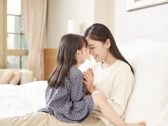 loving asian mother and cute daughter sitting in bed at home