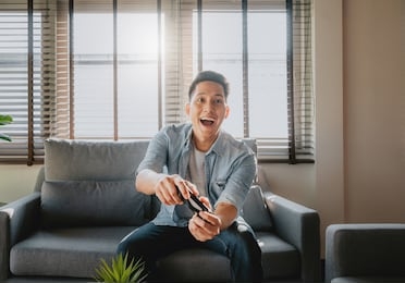 excited asian man looking at tv screen and holding controller while playing video game at home in living room