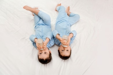 two baby twin boys in pajamas lie on the bed drinking milk from bottles. view from above. concept of marriage and friendship. concept of baby food.space for text
