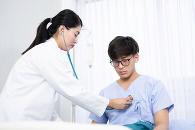 asian doctor using stethoscope checking heart rate in hospital. doctor checking heart rate to diagnose patient's illness & consider medication. asian physician and patient & health insurance concept.