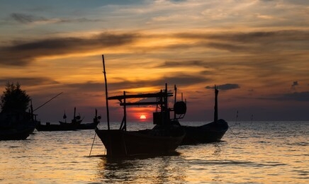silhouette of fishery wooden boat with warm and sunset low lighting dark shadow view.