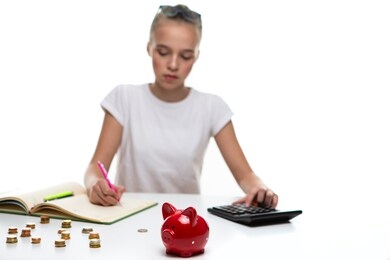 money saving concepts. teenager blond girl posing with coins and moneybox. calculating income with calculator for savings. focus on piggy bank. horizontal composition
