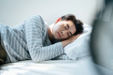 a man sleep on the white bed, the alarm clock wake him up in the morning.